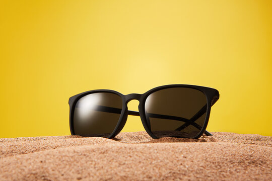 Rimmed sun glasses is on sand on yellow background.