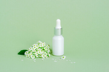 White serum bottle and small white flowers on green background. Skin care, natural cosmetics concept. Closeup