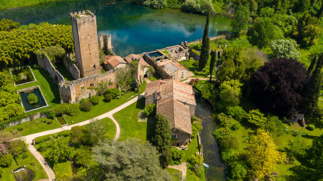 Aerial view of the ruins of the castle and tower located in the garden of Ninfa, near Latina, Italy. The park is an Italian natural monument and contains a lake and a river. It is empty.