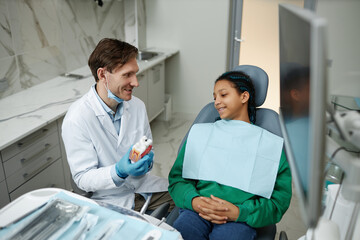 Obraz premium High angle portrait of smiling teen girl in dental chair listening to dentist at consultation