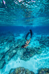 A young woman in bikini free dives above a coral reef in clear tropical water