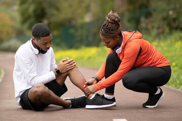 Obraz na płótnie Canvas Serious young african american man doing massage to lady after leg muscle injury, accident at jogging