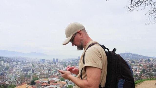 Male tourist taking a picture of cityscape using smartphone. Handsome caucasian man takes a photo with his cellphone of the blurry aerial view of an old european city.
