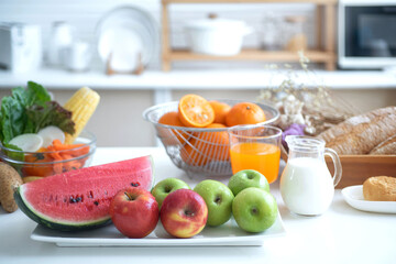 Variety of fresh fruits, vegetables and eggs on table in modern kitchen, a glass of milk and orange Juice