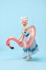 Portrait with funny beautiful princess, queen wearing dress holding pink inflatable flamingo and...