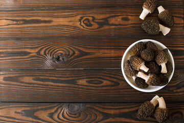 spring morel mushrooms in a plate on a dark wooden background on the right, copy space