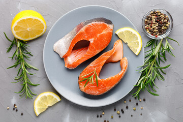Steak of fresh raw red fish salmon with lemon, rosemary and pepper on grey background