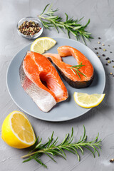 Steak of fresh raw red fish salmon with lemon, rosemary and pepper on grey background