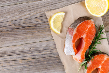 Steak of fresh raw red fish salmon with lemon, rosemary and pepper on wooden background