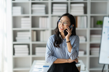 Modern working lifestyle, Asian businesswoman using mobile phone to contact Talking with business colleagues online using internet, smiling happily in office.