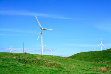 Landscape of green hills and turbine windmill field against blue sky and white clouds. Concept of alternative energy and sustainability. Palmerston North, New Zealand