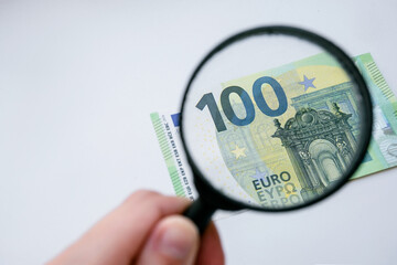 Magnifying glass and euro currency on a white background. 100 euro banknote view through a magnifying glass. Hand holding the lens