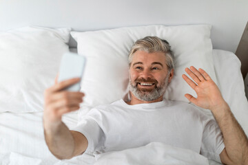Top view of happy man using phone in bed