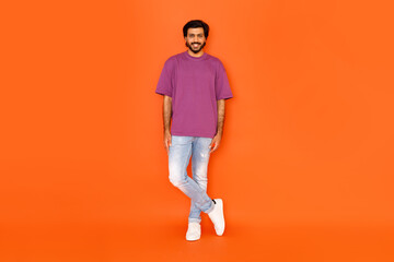 Fototapeta na wymiar Stylish positive hindu guy posing on orange studio background