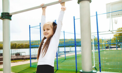 Children and healthy physical activities simple concept. Active little girl, fit sporty child outdoor exercise, hanging on a bar on a playground. Lifestyle.