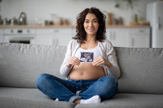 Beautiful Young Pregnant Woman With Baby Sonography In Hands Posing At Home