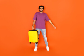 Cheerful young indian man with luggage posing on orange