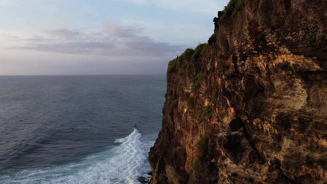 Drone shot flying down the past cliff towards the ocean in Uluwatu, Bali.