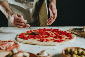 Close-up of chef preparing pizza putting tomato sauce on the dough