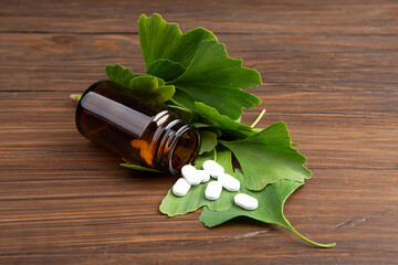 Bottle of pills and fresh ginkgo biloba leaves on wooden background. Traditional, herbal medicine and Homeopathy concept.