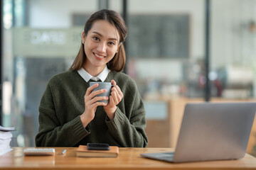 Beautiful and confident Asian businesswoman holding a cup of coffee to drink during break Relax...