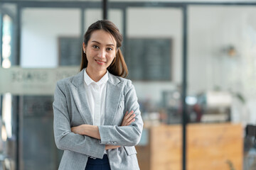 Attractive asian businesswoman standing with crossed arms and looking at camera in office confident and happy with business success