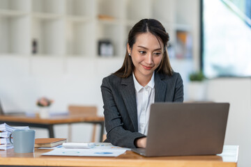 Young Asian businesswoman holding a pen sitting and analyzing the details of management information Finance is happy at the desk in the office. © crizzystudio