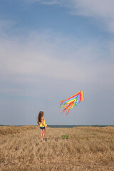 A child launches a colored rainbow kite into the sky in a field on a sunny summer morning