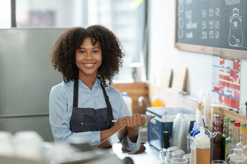 Beautiful african american female cashier or barista writing purchase details and checking...