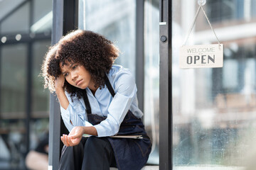 African barista woman in a barista uniform holding file showing stress and frustration sitting the...