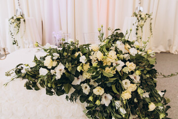 Wedding. Banquet. Decor. The festive table is decorated with a composition of white flowers and leaves of greenery. There are candles, glasses and plates on the table.