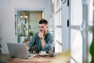 A male caucasian, Handsome Freelancer bearded man in t-shirt taking notes at laptop sitting at desk. freelance concept.