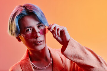 Portrait of stylish young guy with blue hair looking at camera against colored neon background