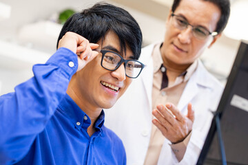 Senior experienced male optician offering the glasses frames to young man client, optometrist giving new glasses.