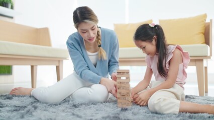 Happy little daughter play toy wooden block with mother spending time together on holiday in living...