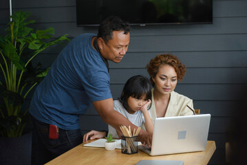 Asian mother, father, and Daughter using laptop together. Thai Woman, man, and Child talk on video call and learn online study at home. Happy family concept.