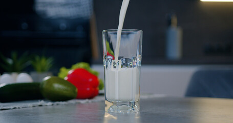 Somebody is filling natural milk into transparent glass which standing on surface of table in contemporary cuisine