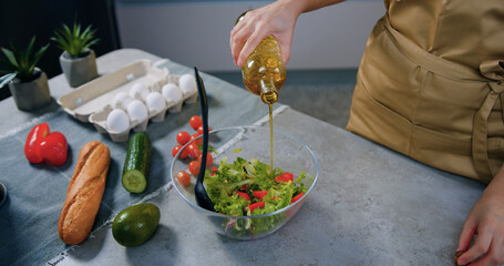 Unrecognizable housewife adding olive oil into vegetable salad in glass bowl when preparing it in contemporary kitchen,homemade preparation concept