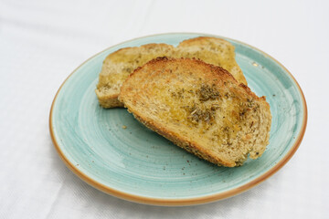 toasted bread with olive oil, herbs and garlic salt on a blue plate, copy space, selected focus, narrow depth of field