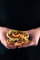 Shawarma from beef, avocado, onion, pickled cucumbers, sauce and pita bread in hands on a black background.