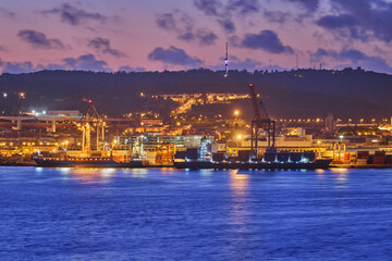 Fototapeta na wymiar View of Lisbon port with sea container ships with port cranes in the evening twilight over Tagus river. Lisbon, Portugal