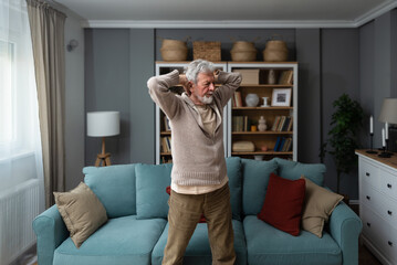 Sporty elderly guy practicing yoga indoors. Senior man doing stretching exercise at home. Active lifestyle and healthcare in any age. Old retired person light fitness training in living room - Powered by Adobe