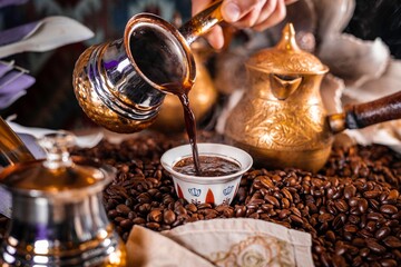 Turkish coffee being served in beautiful mugs in a table covered with coffee grain beans with gold teapots as decoration