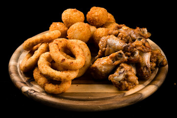 Snack fried chicken legs, breaded mozzarella cheese balls and crispy squid rings breaded (caramari) on dark background.