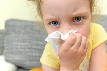 The child has a cold. He wipes his nose with a tissue. Strong runny nose.