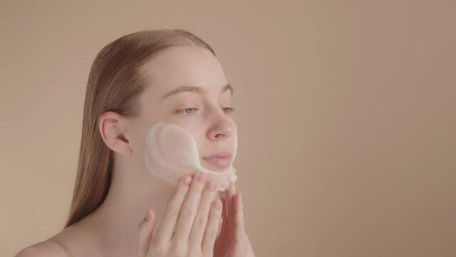 Young Caucasian blonde lady, isolated background, using face wash foam
