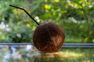 Texture for background. Large brown coconut with a tube lies on the glass against a blurred background of green grass. Selective focus.