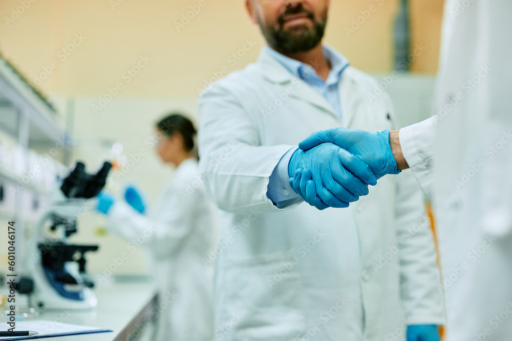 Wall mural close up of scientists shaking hands while working in laboratory.