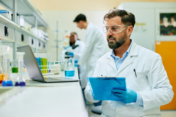 Male scientist taking notes while analyzing medical data on laptop in laboratory. - Powered by Adobe