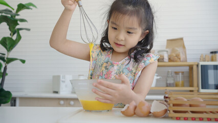 Asian mother and daughter in kitchen break eggs and beat eggs in glass bowl.